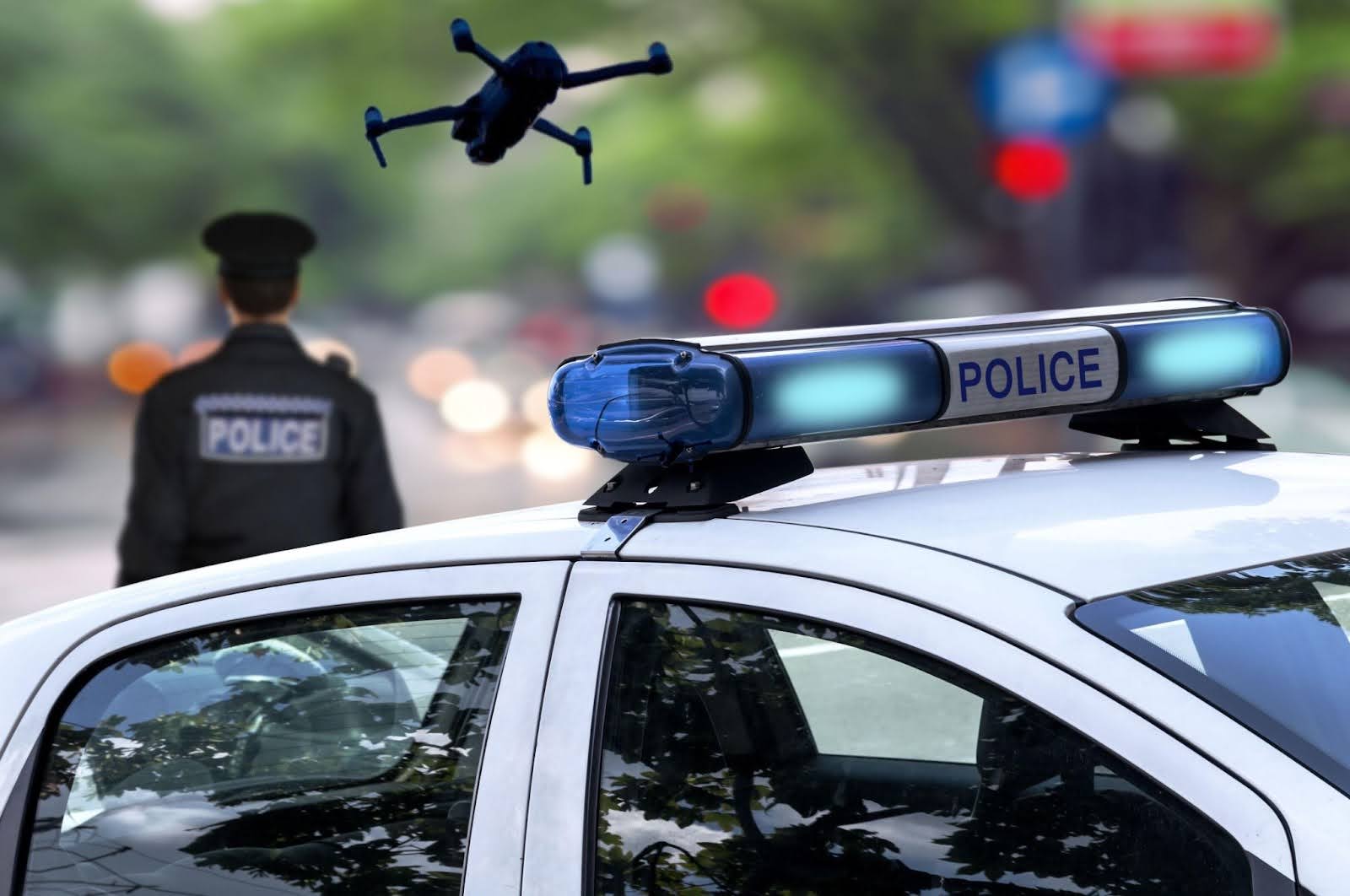 Police car and officer with a drone overhead, showcasing Counter-Unmanned Aerial Systems technology in law enforcement.